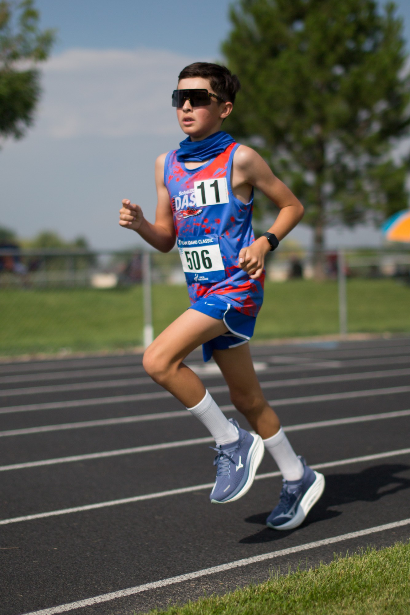 A DASH runner in sunglasses and a neck gaiter running past trees
